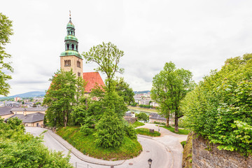 View of old catholic church in salzburg, green and red roof, winding road and trees, rainy day, austria