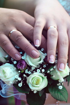 hands of the bride and groom with rings on wedding bouquet