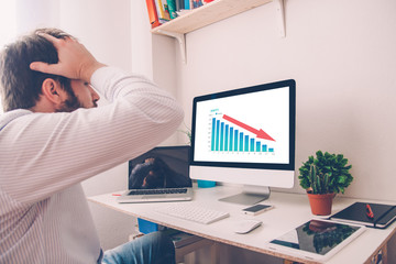 Man with hands on the head in front of computer with graph of unsuccessful business on the screen.