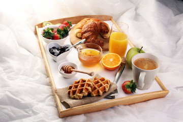 breakfast in bed with fruits and pastries on a tray -waffles, croissants, coffe and juice