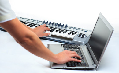 man playing on a synthesizer and writes on a laptop