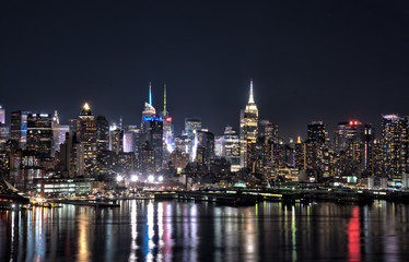 New York city skyline at night with building lights reflected in Hudson River