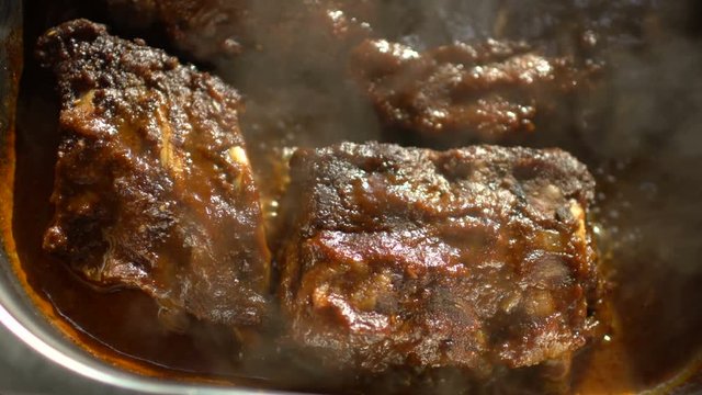 Rotating of hot meat dishes with pork ribs with gravy boiling sauce at restaurant kitchen