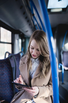 Beautiful young woman sitting in city bus and looking at tablet.