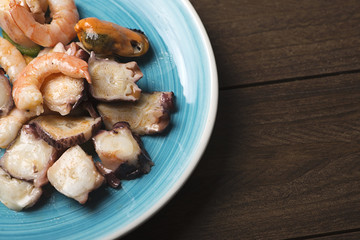 Tasty seafood salad over blue plate and brown wooden table. Horizontal shoot.