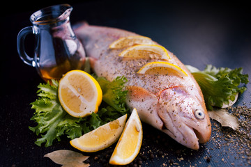 Fresh trout and ingredients to prepare fish dishes on black table