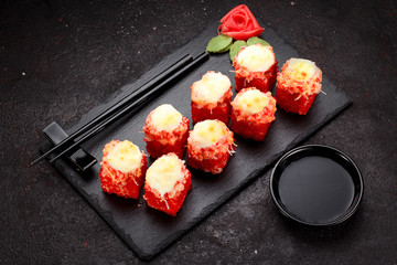 Japanese cuisine. Baked (hot) sushi roll on a stone plate over black concrete background.