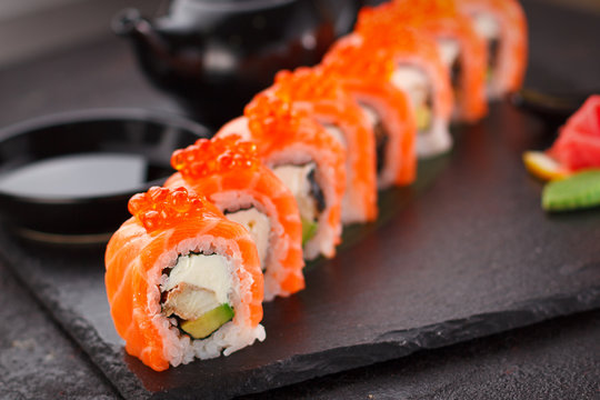 Japanese cuisine. Salmon sushi roll on a stone plate over concrete background.