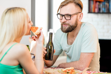Young couple dressed casually having a lunch with pizza and beer at home
