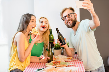 Young friends dressed casually in colorful t-shirts making selfie photo with pizza and beer at home