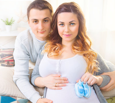 Happy young couple expecting baby. Beautiful pregnant woman and her husband together caressing her pregnant belly
