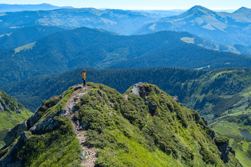 Traveler stands on a ridge, on a background of green mountains
