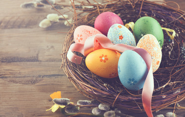 Easter background. Beautiful colorful eggs in nest with spring flowers over wooden brown background border design