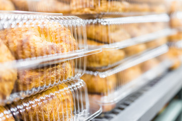 Many plain croissants packaged in plastic boxes on display in store