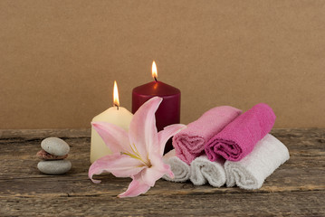 Beautiful composition with two candles, stack of spa stones and towels on wooden background, with pink lily flower, spa treatment concept