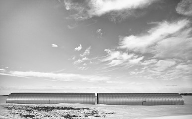 Two industrial steel culverts laying on snow covered field in a black and white winter landscape - obrazy, fototapety, plakaty