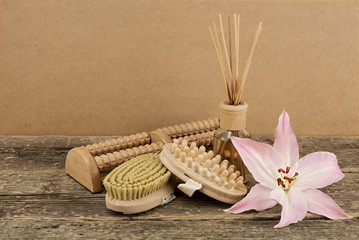 Beautiful composition with aromatic oil, pink lily and massage brushes on wooden background, weight loss and bodycare concept