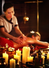 Massage of woman in spa salon. Girl on candles background treats problem back spa salon. Luxary interior with working masseuse . Shirodhara Pot background. Female bare back has relax .