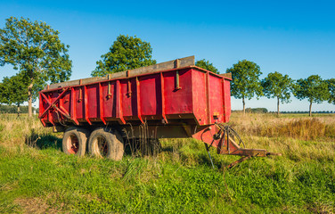 Old red colored farm trailer in the field