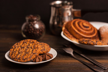 oatmeal cookies on a saucer and a cinnamon roll, coffee beans in a jar