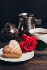 a red rose lies on a saucer with a cupcake, a drink in a cup, a ladle and a jar with coffee beans