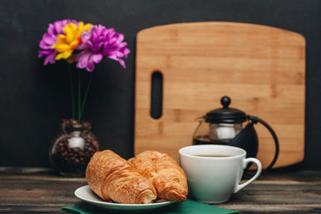 croissants on a saucer, a cup with a drink, a cutting board and a vase of flowers