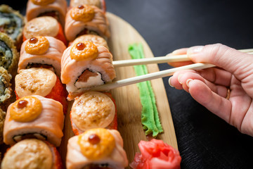 Hand with chopsticks on sushi roll set with wasabi and ginger on cooking desk. Flat lay, top view.
