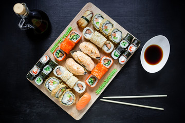 Fototapeta na wymiar Japanese food, catering, roll plate or platter set. Sushi roll with chopsticks, ginger, soy sauce, wasabi at dark background. Top view. Flat lay