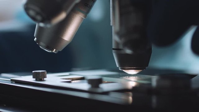 Close up view of scientist hands with gloves set the sample in the microscope for research