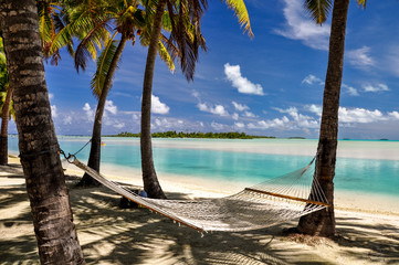 Stunning view of a beach in the lagoon of Aitutaki, Cook Islands, in the South Pacific Ocean. Clear water, palm trees, a white sand beach and a large hammock between palm trees on a sunny day.