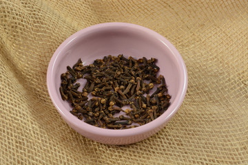 Whole cloves spice in pink dish on burlap