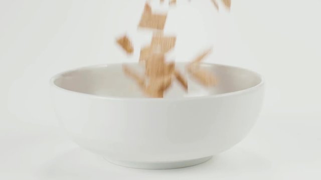 Dry cereal tumbles in slow motion into a bowl on a white cyc