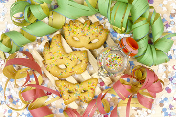 carnival masks of short pastry with streamers on wood background