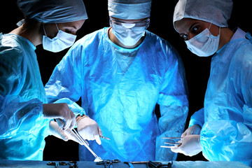 Medical team performing operation. Group of surgeon at work in operating theatre toned in blue.