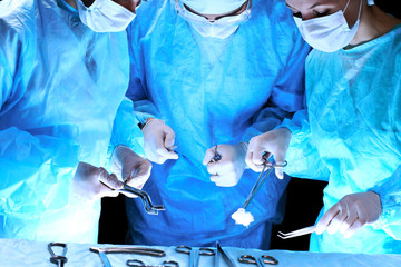 Medical team performing operation. Group of surgeon at work in operating theatre toned in blue.