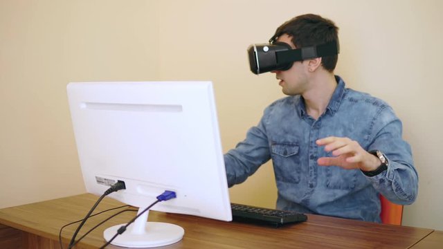 Young programmer works with VR glasses on while sitting near his personal computer. Shot in 4K.