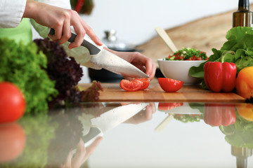 Closeup of human hands cooking vegetables salad in kitchen on the glassr table with reflection. Healthy meal and vegetarian concept