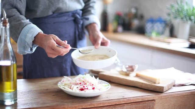 Woman spooning salad dressing on cut-up vegetables