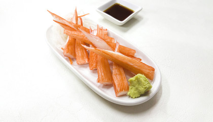 Crab sticks and wasabi in white saucer on table