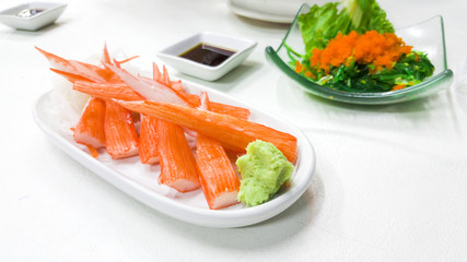 Crab sticks and wasabi in white saucer on table