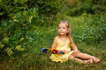 Cute little girl holding a pinwheel. She sits on the lawn. A walk in the summer park. Summer vacation. Outdoor Activities.