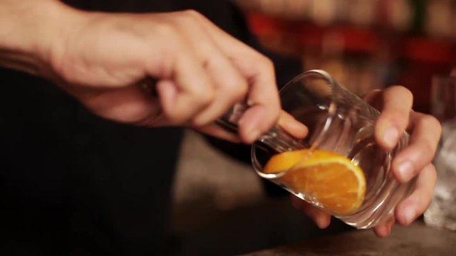 Bartender muddling orange slice