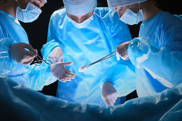 Group of surgeons at work in operating theater toned in blue. Medical team performing operation