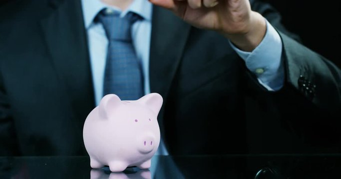 A man dressed in a suit and tie, puts money into the piggy bank. Concept: Pension, savings, investment, accumulation plan, savings for college studies.