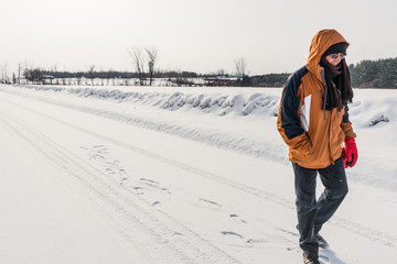 Man walking in snow on country road, Canada