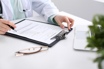 Fototapeta premium Close-up of a female doctor filling out application form , sitting at the table in the hospital