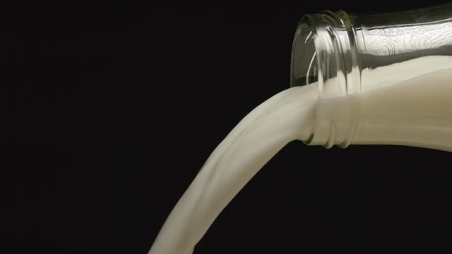 SLOW MOTION: Milk flows from a neck of bottle on black backgrounds - Side view