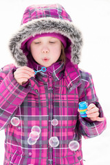 Little girl blowing bubbles in snow