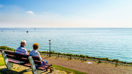 Senior couple enjoying a rest and view of the inland sea named IJselmeer with its wind farms from the historic fishing village of Urk in the Netherlands - obrazy, fototapety, plakaty