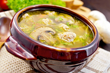 Soup with meatballs and mushrooms in clay bowl on board